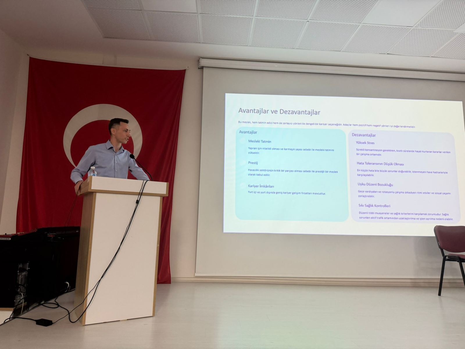 Sunumun "Avantajlar ve Dezavantajlar" bölümüne odaklanan bu karede, genç bir konuşmacının kürsüdeki dinamik anlatımı görülüyor. Ekranda mesleki tatmin, prestij ve kariyer imkanları gibi başlıkların yer alması, söyleşinin bilgilendirici içeriğini net bir şekilde ortaya koyuyor.